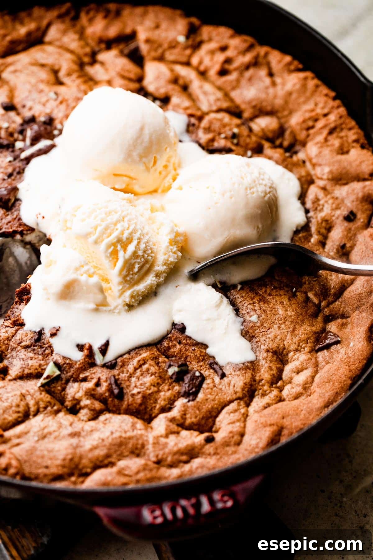A vibrant close-up overhead shot of a delightful mint chocolate skillet cookie, generously topped with three scoops of creamy vanilla ice cream, creating an inviting dessert scene.