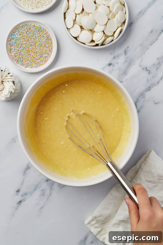 Yellow cake batter in a mixing bowl with a whisk, showing the initial stages of preparation.