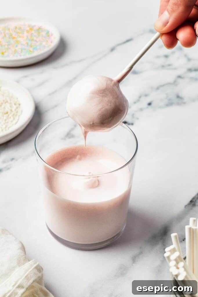 A perfectly round cake ball being carefully dipped into a glass of smooth, melted candy coating.