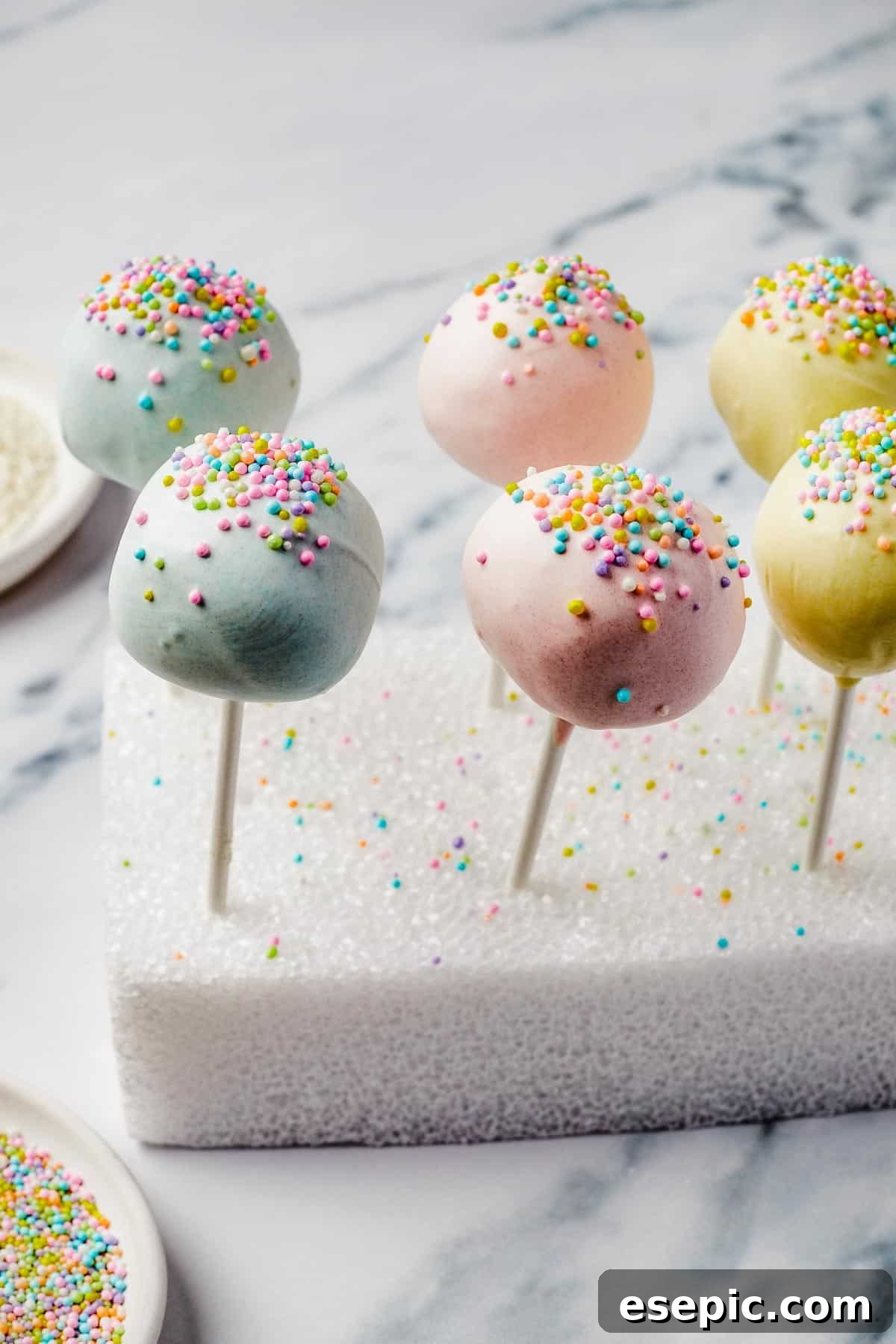 Lollipops cake pops adorned with colorful sprinkles, meticulously drying in a styrofoam block.