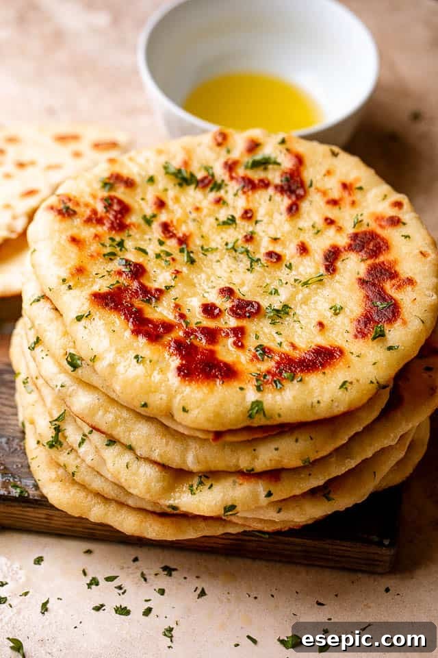 Top view of a stack of homemade flatbread on a wooden board next to a bowl of olive oil, ready to be served.