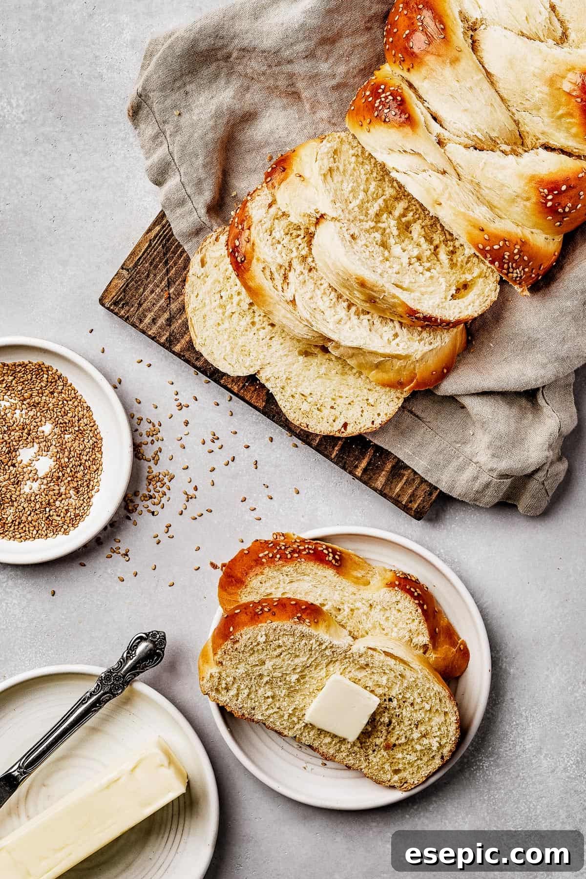Fluffy, Golden, and Irresistible Challah Bread 11 Overhead shot of a wooden cutting board with a tea towel, displaying perfectly sliced braided challah bread.