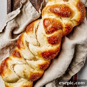 Fluffy, Golden, and Irresistible Challah Bread 12 Baked challah with sesame seeds, on a sheet pan with a tea towel.