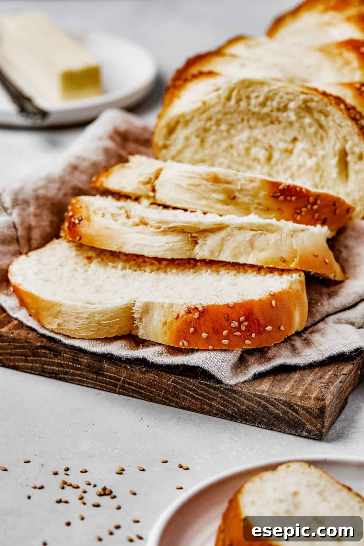 Fluffy, Golden, and Irresistible Challah Bread 4 A beautifully braided and sliced challah bread on a wooden cutting board with a tea towel.