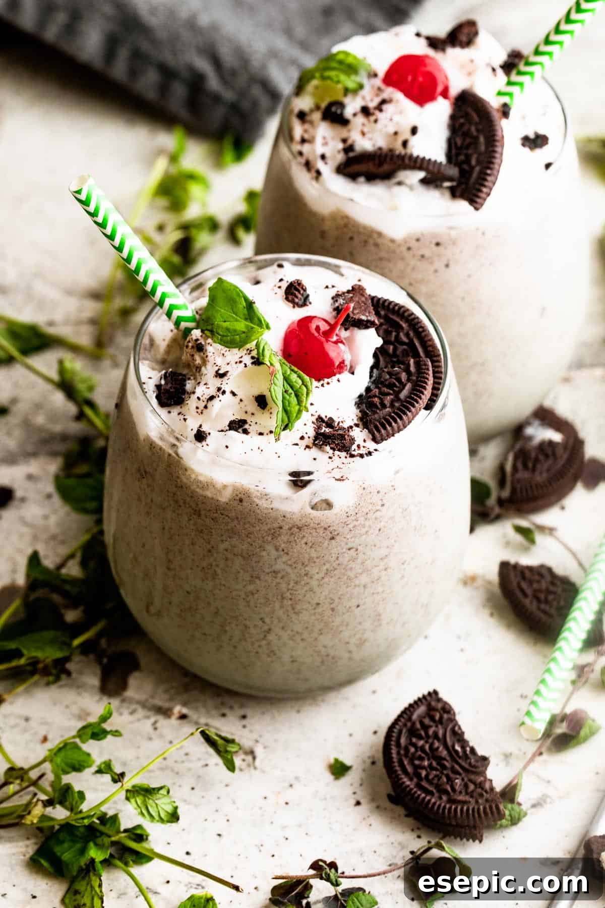 Shamrock Oreo Dream Swirl 3 two drinking glasses filled with Shamrock Oreo McFlurry Shake, topped with whipped cream, maraschino cherries, and mint leaves.