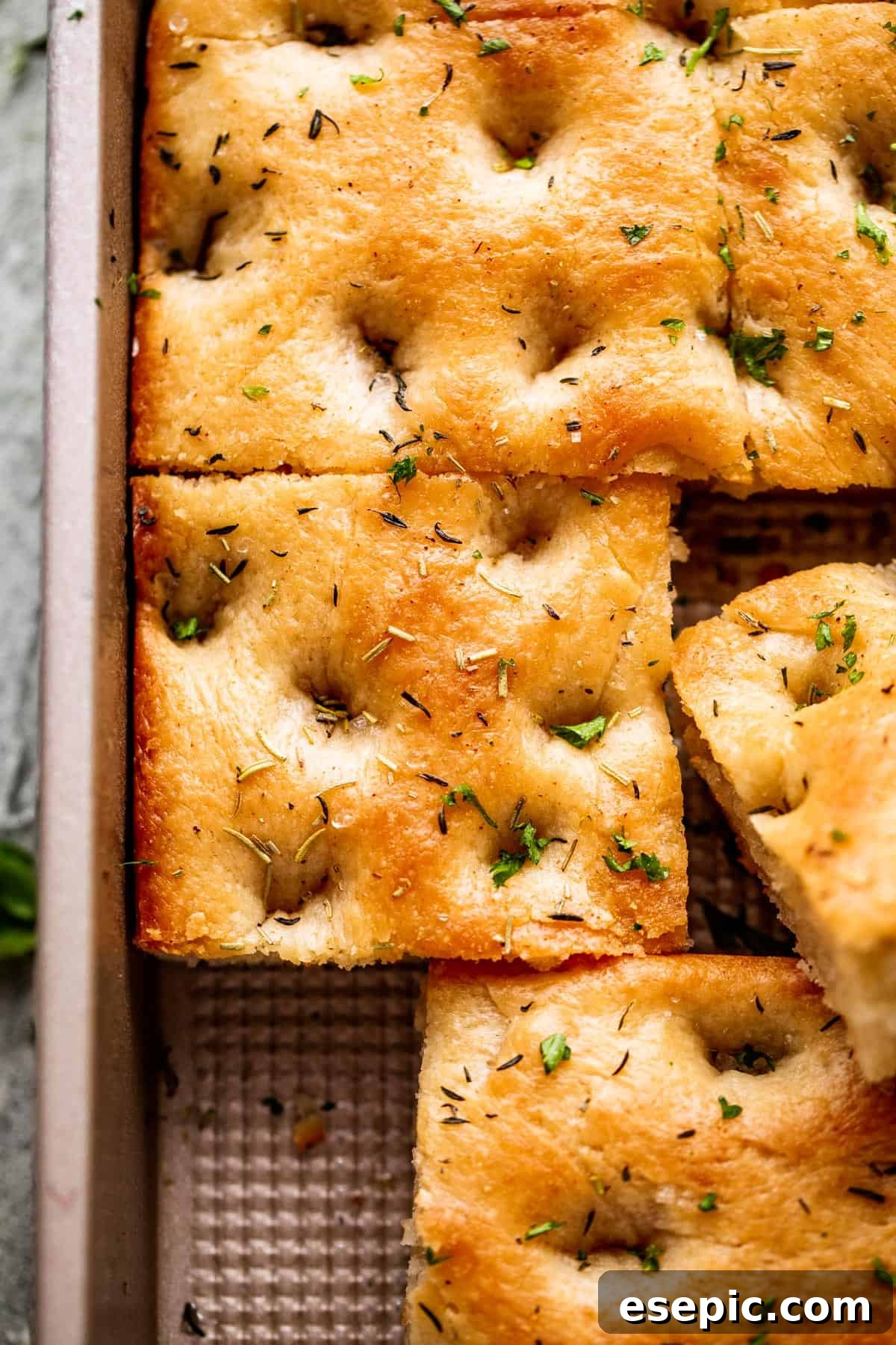 Aromatic Garlic and Herb Focaccia 3 A large pan-sized loaf of focaccia, with one corner neatly cut away, highlighting its inviting texture.
