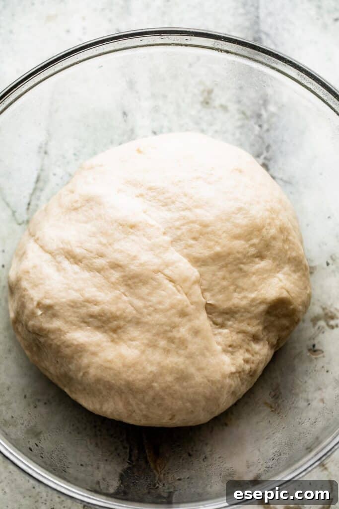 Aromatic Garlic and Herb Focaccia 5 A glass bowl holding a perfectly smooth ball of risen bread dough, coated in olive oil.