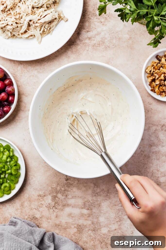 A small mixing bowl with creamy chicken salad dressing, being whisked.