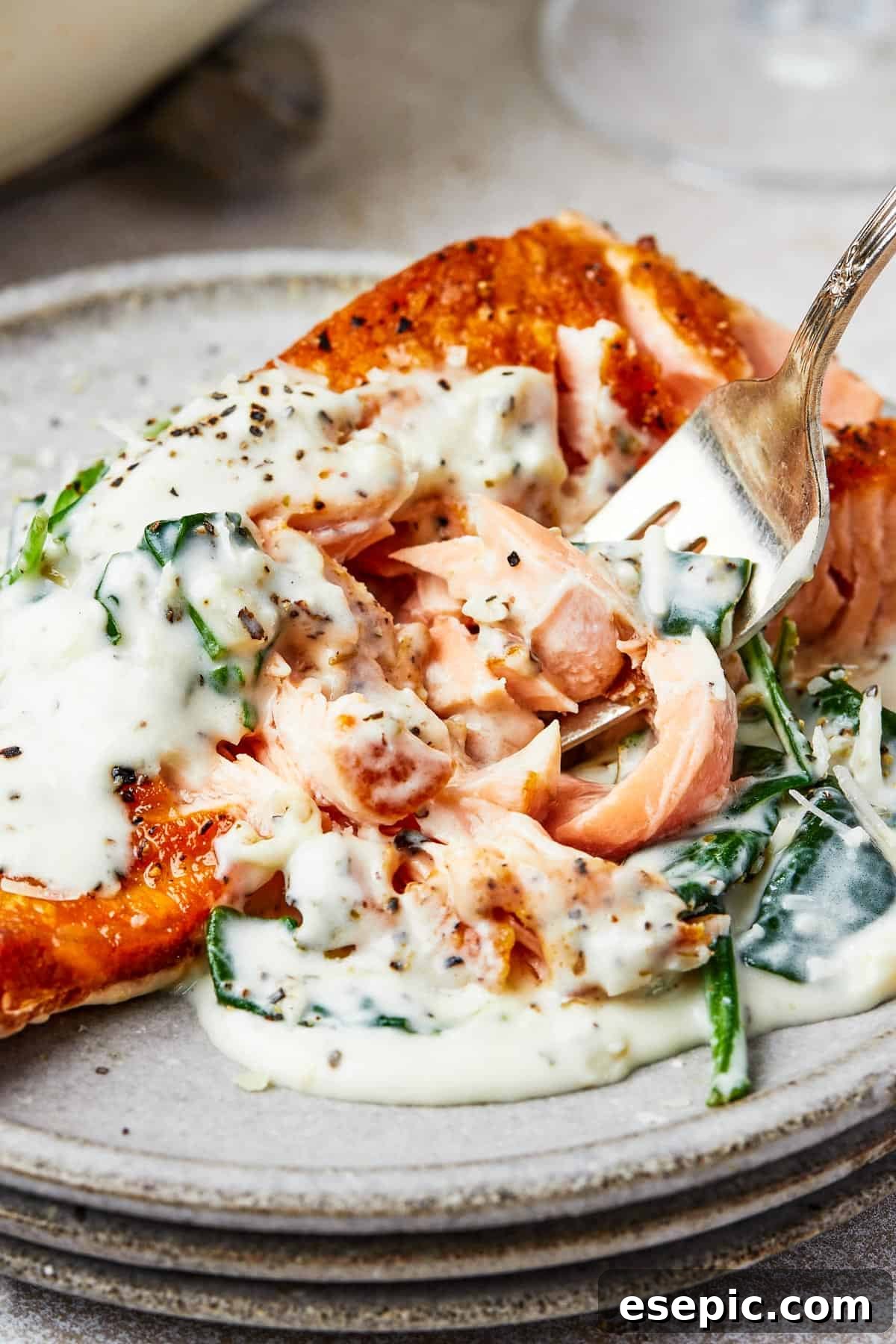 A serving of perfectly cooked Salmon Florentine, with a fork lifting a bite of salmon towards the camera, showcasing the creamy spinach sauce.