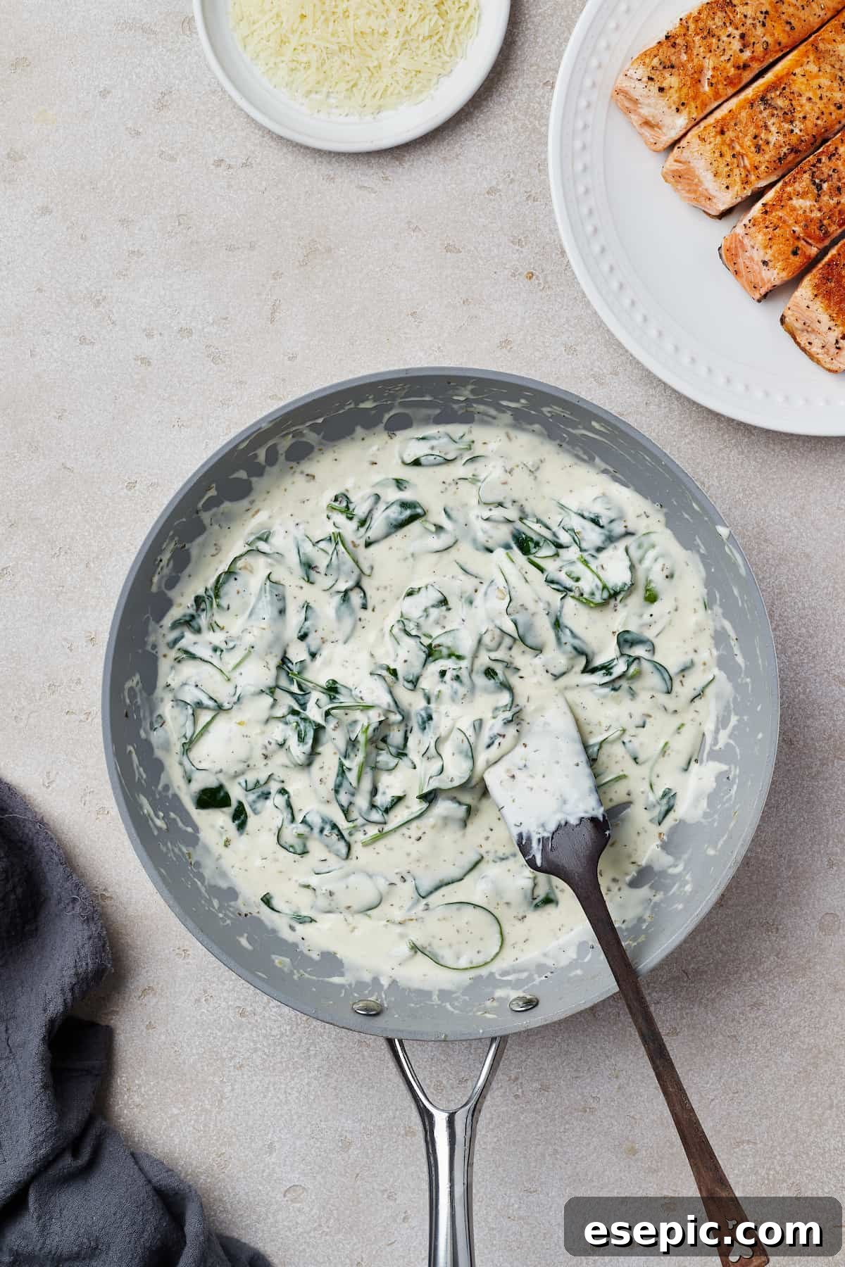 A vibrant, creamy spinach sauce simmering in a nonstick skillet, rich with herbs and ready for the salmon.