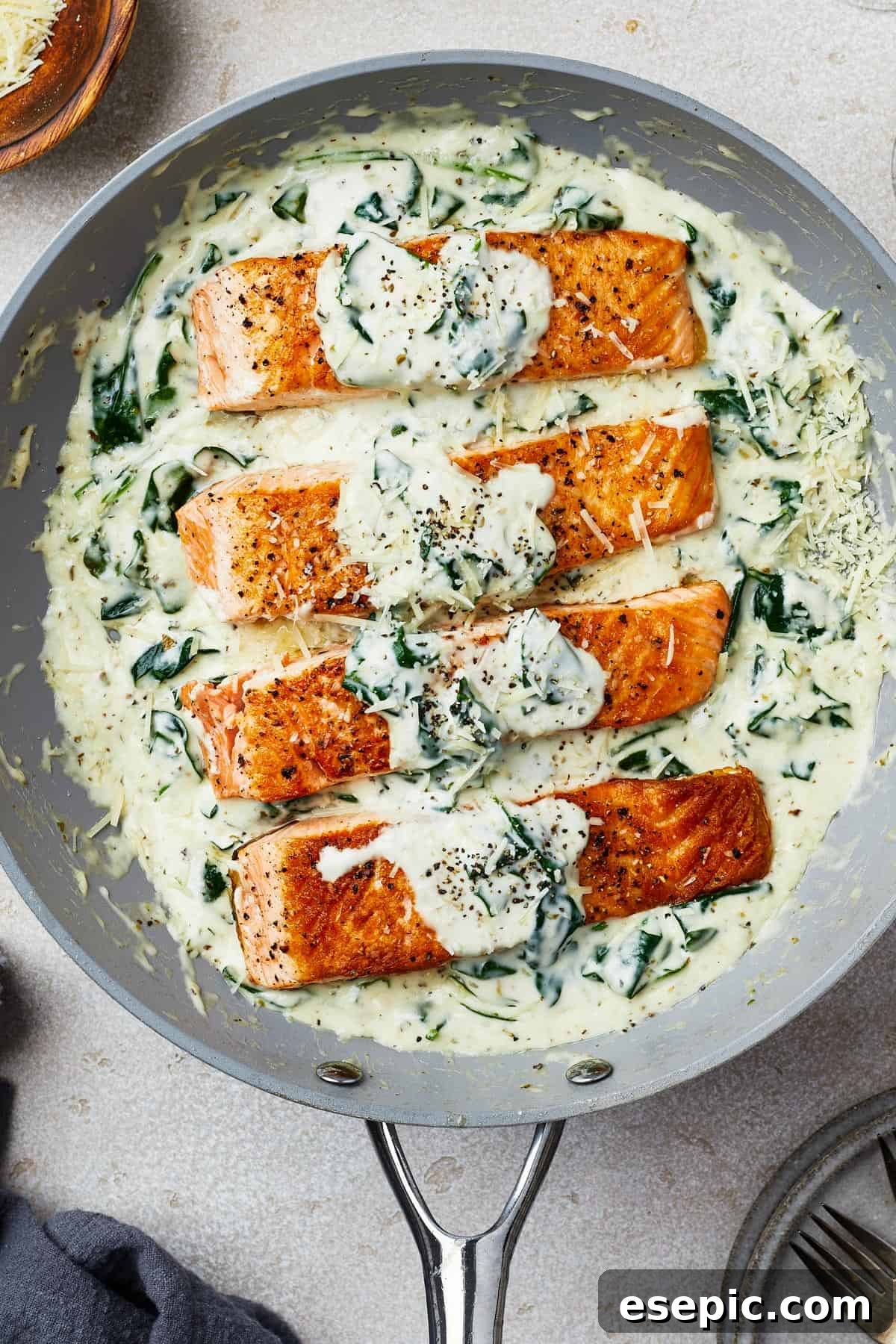 Succulent salmon fillets perfectly arranged in a gray nonstick skillet, generously coated with creamy spinach sauce.