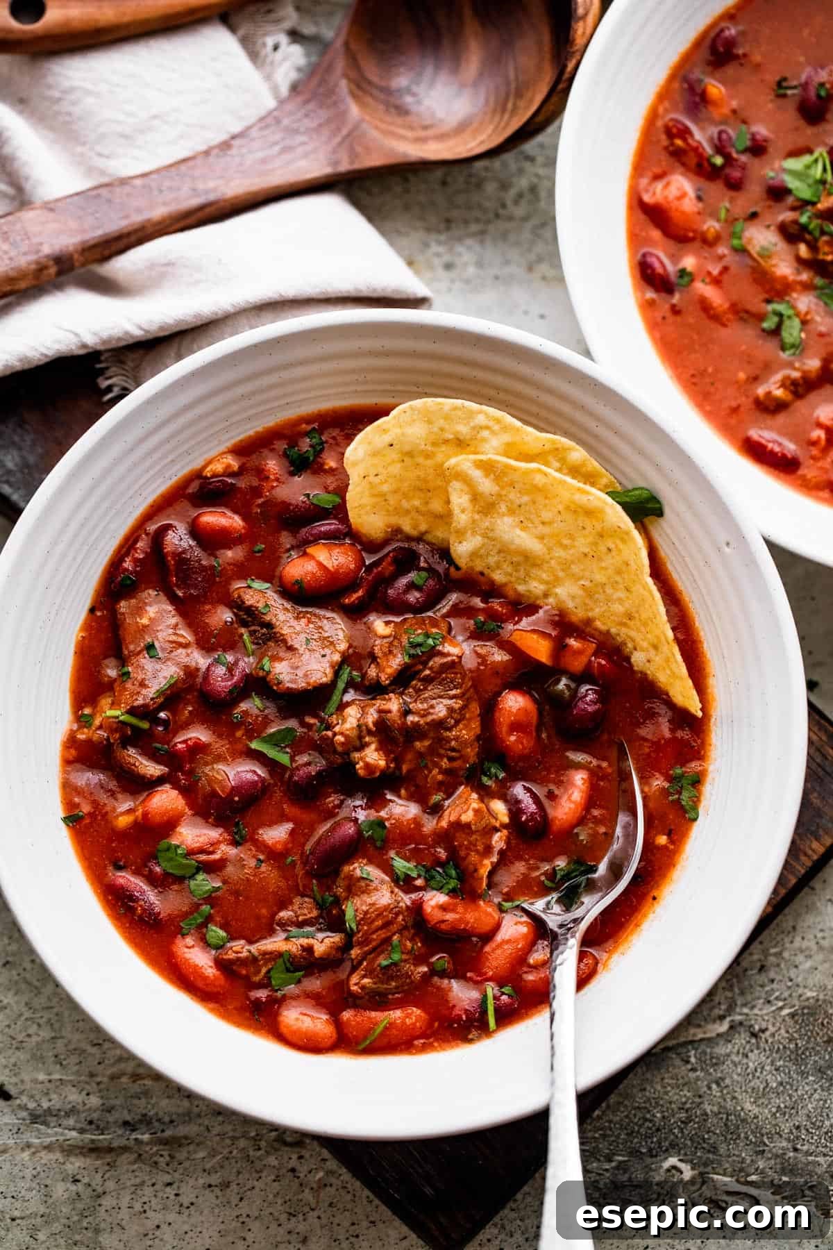 Two white bowls filled with Chili con Carne, with tortilla chips peeking out, ready to be served.