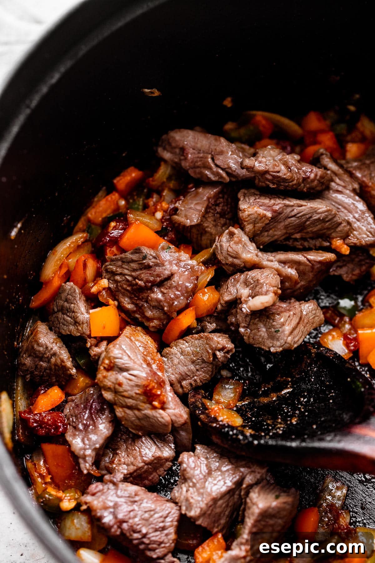 Browning cubed chuck roast pieces and diced vegetables in a dark Dutch oven, building a flavorful base for chili con carne.