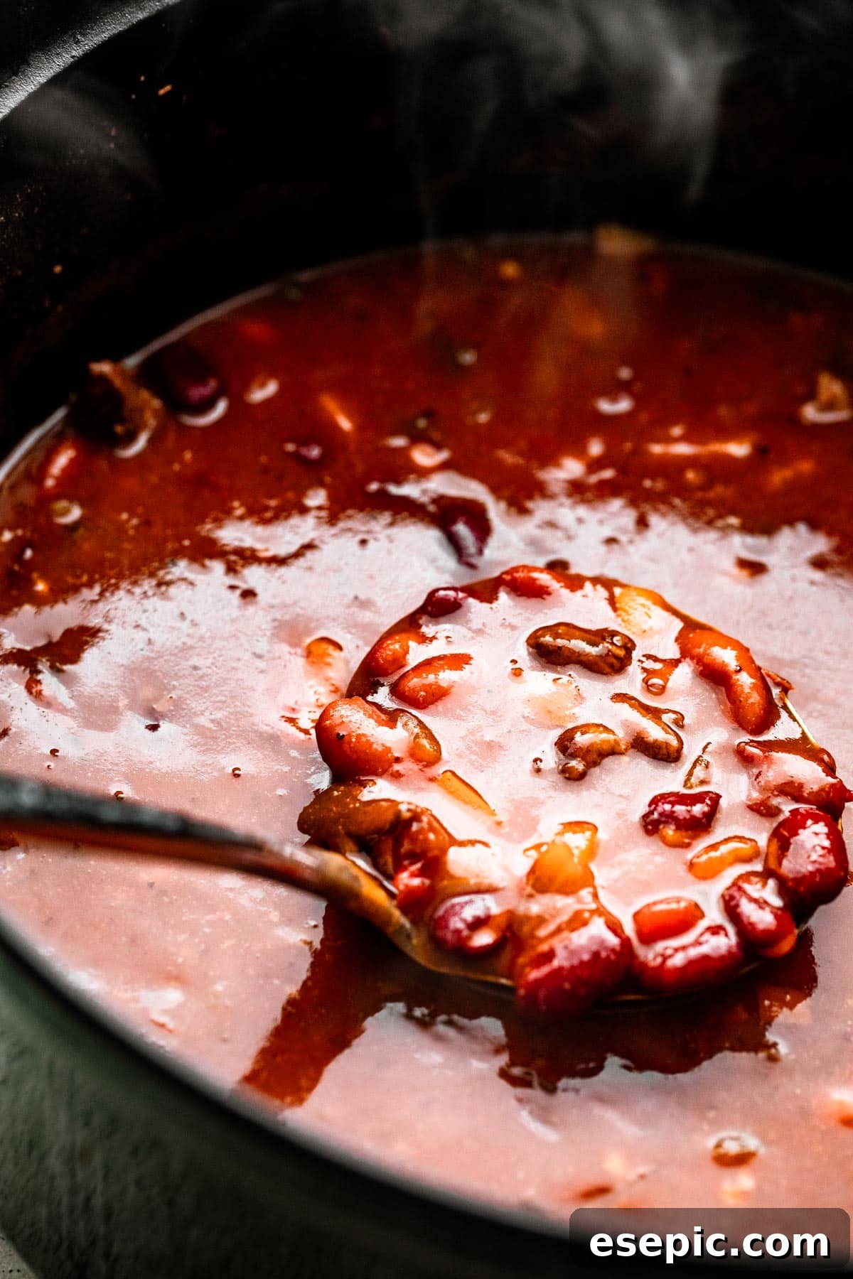 A ladle spooning out thick, hearty Chili con Carne from a dark Dutch oven, showcasing its rich texture.
