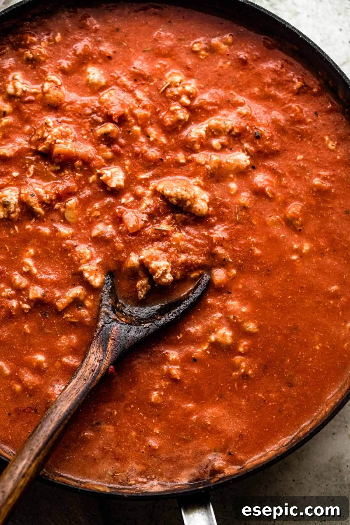 wooden spoon stirring through ground turkey in tomato sauce in a skillet.