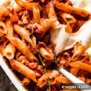 spooning out baked penne pasta from baking dish.