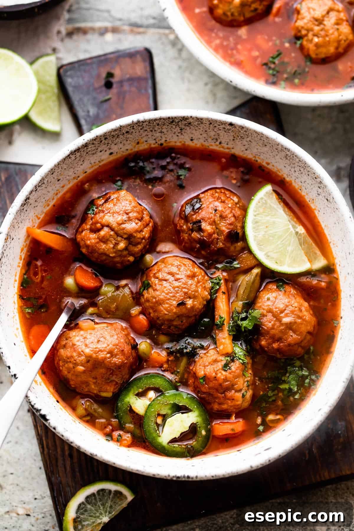 overhead shot of two soup bowls filled with albondigas soup and garnished with limes and sliced jalapenos.