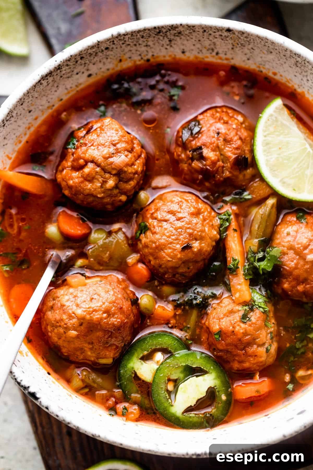 close up overhead shot of soup bowl filled with albondigas soup and garnished with limes and sliced jalapenos.