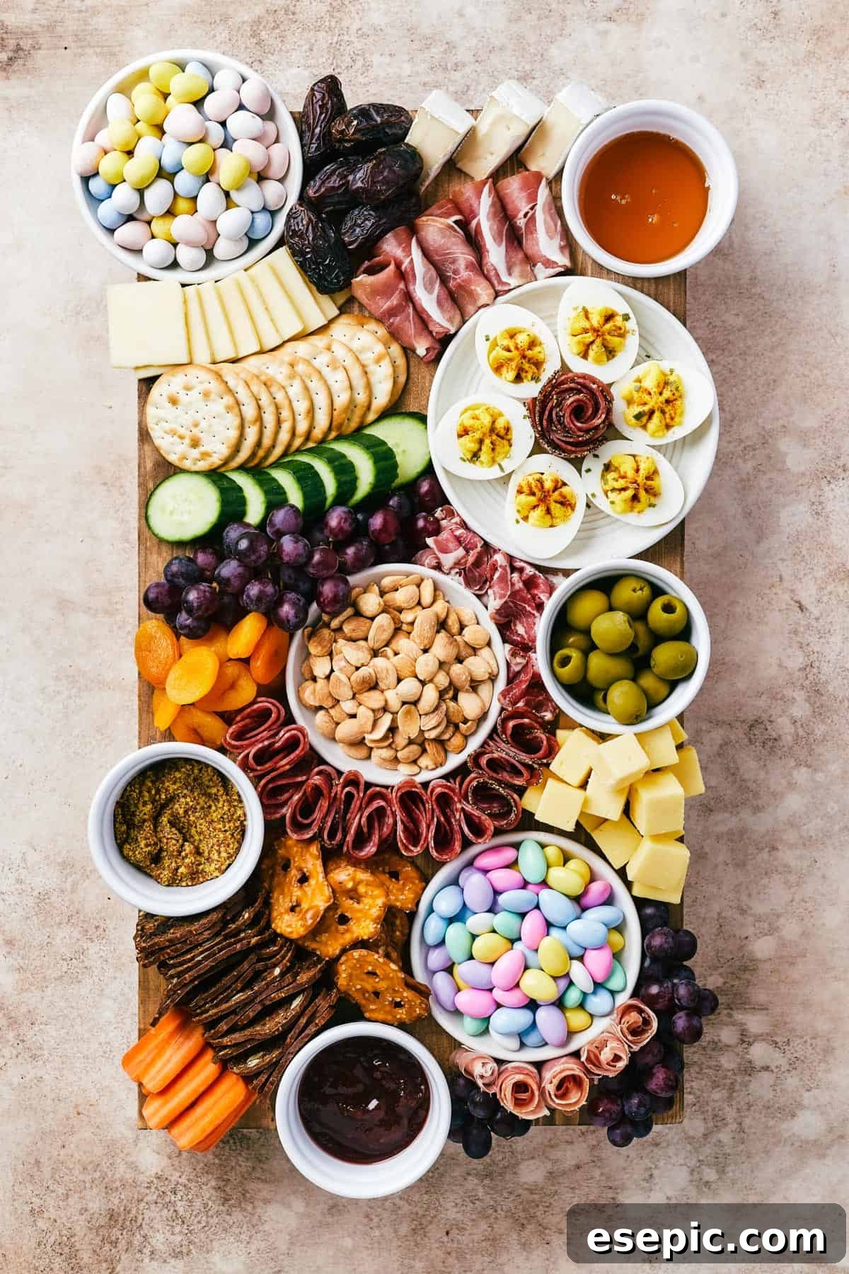 A wooden cutting board artistically arranged with meats, cheeses, crackers, olives, fruit, veggies, and more.