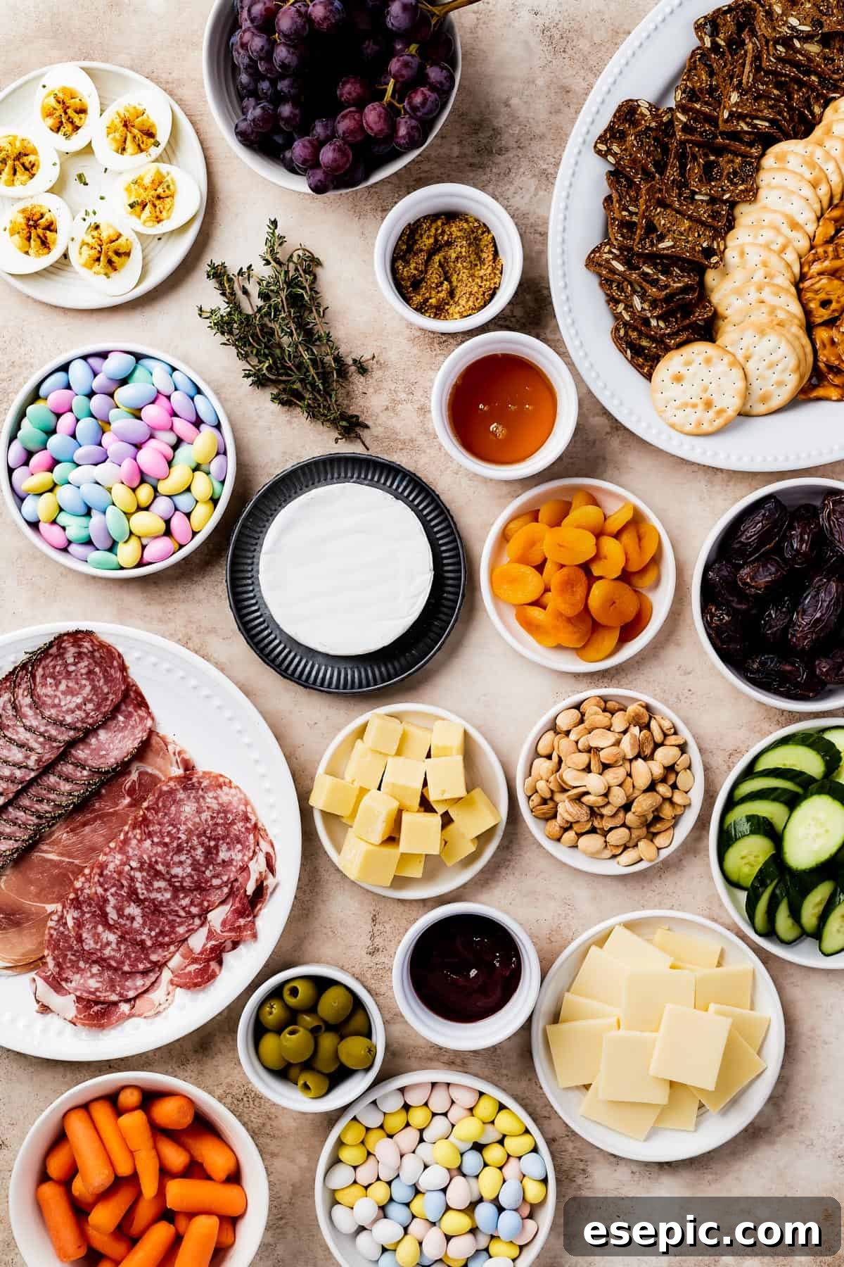 From top left: Deviled eggs, grapes, a platter of crackers, jordan almonds, fresh thyme, grainy mustard, strawberry preserves, a wheel of brie, dried apricots, medjool dates, a plate of sliced meats, cubed white cheddar, marcona almonds, sliced cucumber, castelvetrano olives, honey, gouda.