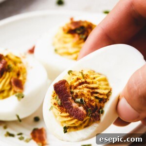 A woman's hand is lifting a deviled egg from a small plate toward the camera.