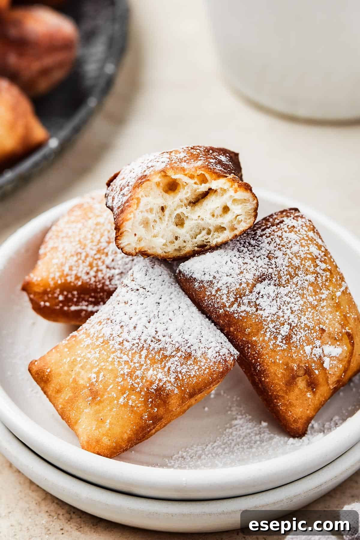 Homemade square donuts presented on a plate. One beignet has been carefully broken in half, revealing its incredibly fluffy and airy interior texture.