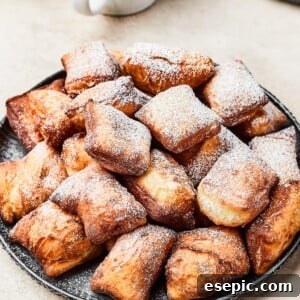 A plate of fried beignets, dusted with powdered sugar.