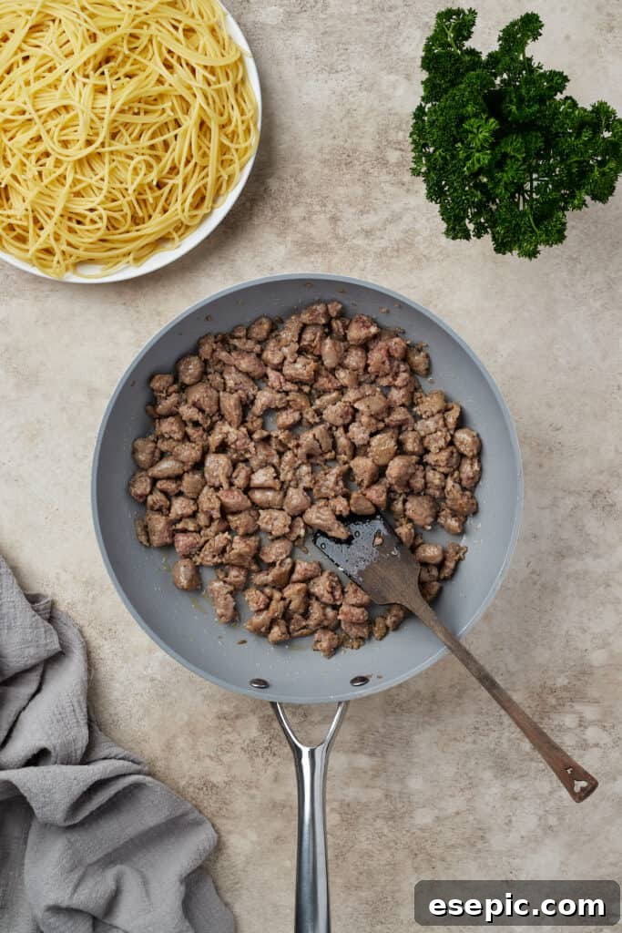 Irresistible Golden Spaghetti Bake 6 Crumbled Italian sausage browning in a hot skillet on a stovetop.
