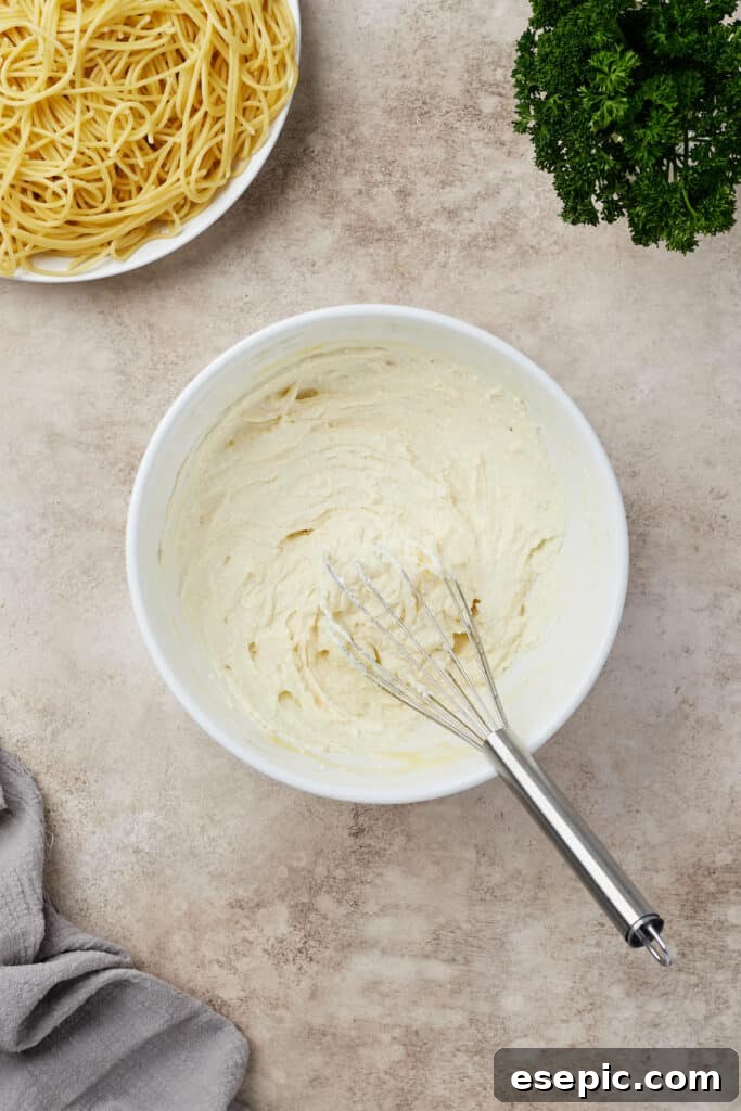 Irresistible Golden Spaghetti Bake 8 Ricotta cheese and an egg are whisked together in a mixing bowl, creating a smooth, creamy mixture.