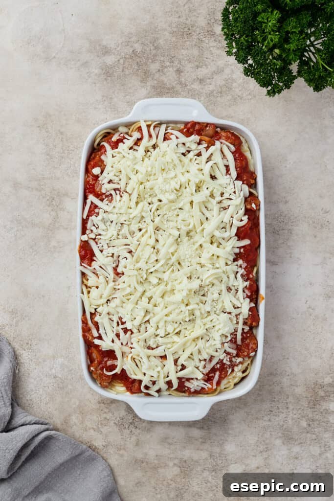 Irresistible Golden Spaghetti Bake 9 A layered, unbaked spaghetti casserole waits in a baking dish, topped with cheese and ready for the oven.
