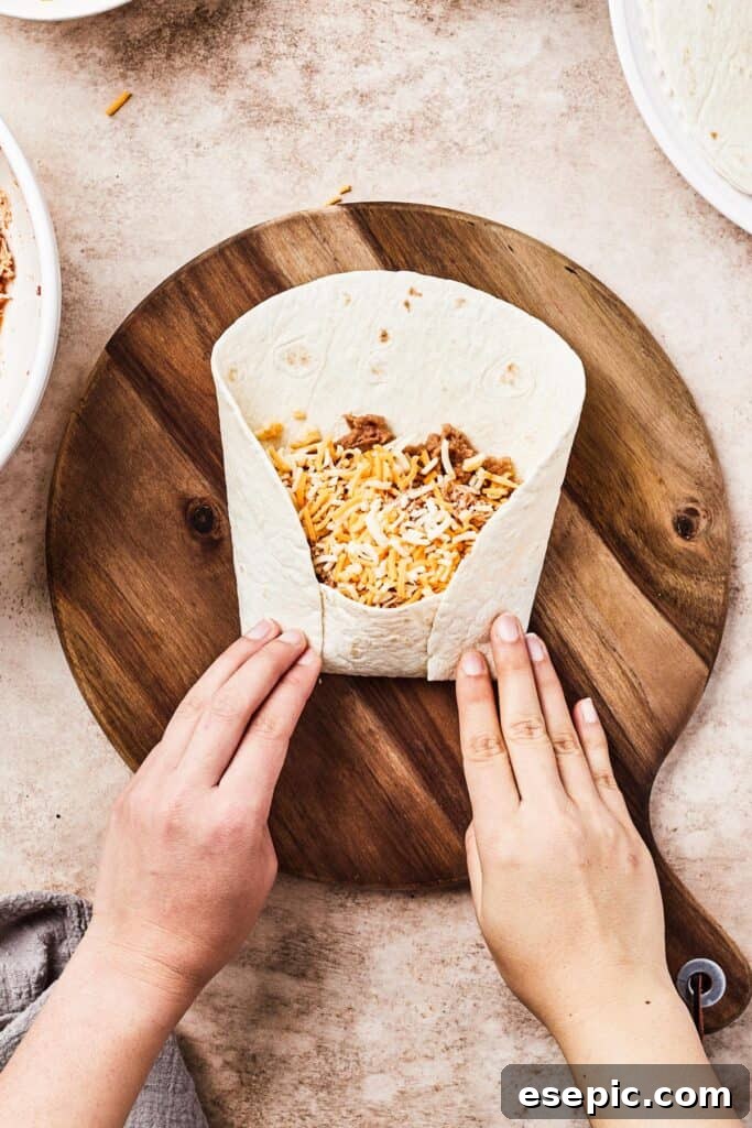 Golden Fried Chicken Chimichangas from Scratch 6 A woman demonstrates how to fold a tortilla, bringing the bottom and sides over the filling to create a tight burrito shape.