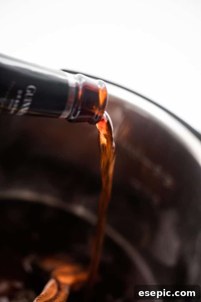 Pouring a dark Guinness beer into the stainless steel insert of an Instant Pot, preparing the cooking liquid for corned beef.