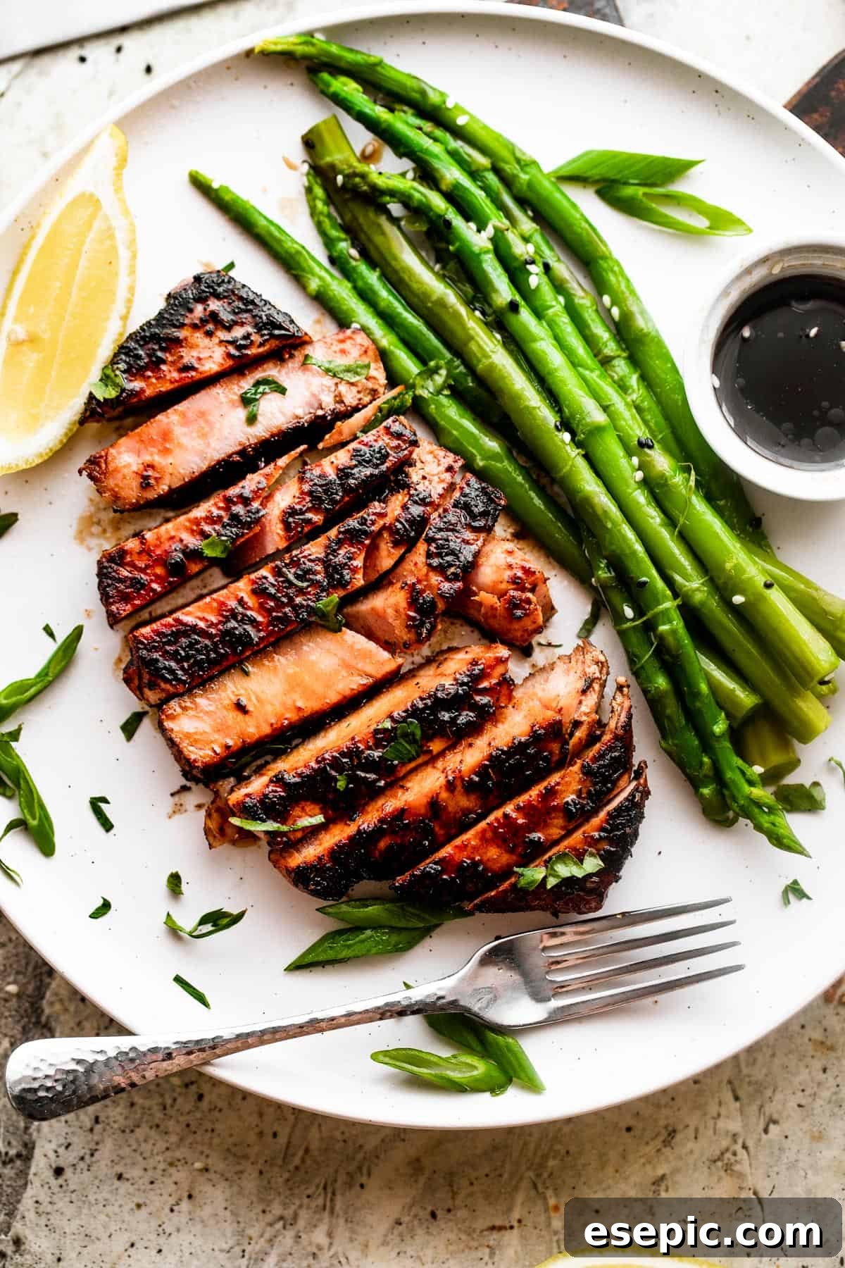 Overhead shot of a sliced tuna steak served on a white dinner plate with asparagus stalks, dipping sauce, and lemons.