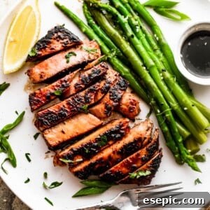 wide overhead shot of a white dinner plate with a sliced tuna steak, asparagus stalks, soy dipping sauce, and a lemon wedge.