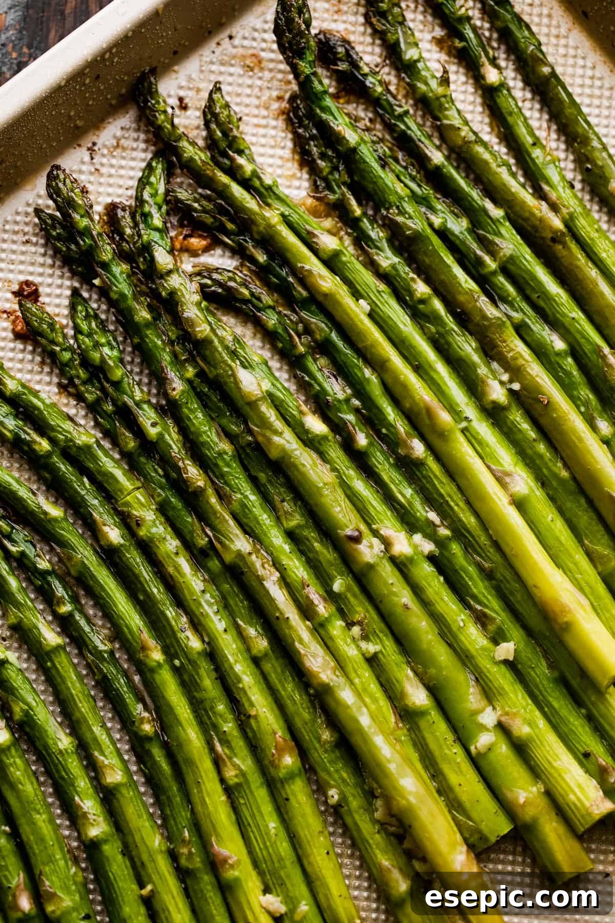 Perfect Garlic Butter Asparagus 6 Close-up shot of individual asparagus spears, perfectly roasted and arranged on a gold-colored baking sheet.