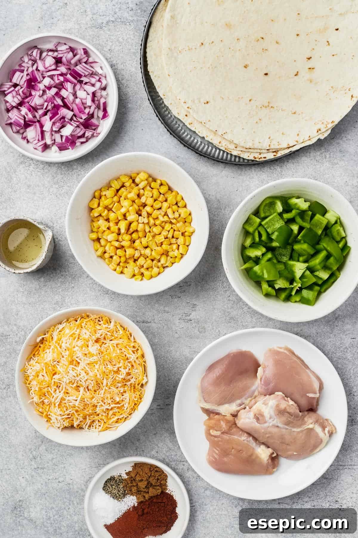 Individual ingredients for chicken quesadillas laid out on a table: Red onion, tortillas, oil, corn kernels, bell pepper, cheese, chicken thighs, and a mix of spices.