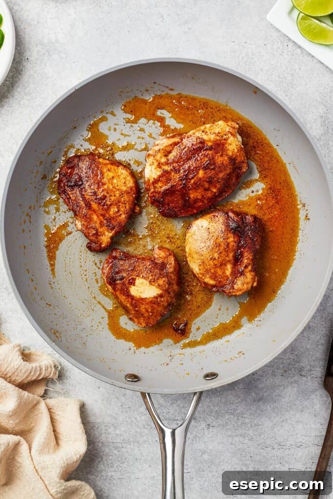 Seasoned chicken thighs cooking in a hot skillet, achieving a golden brown sear.