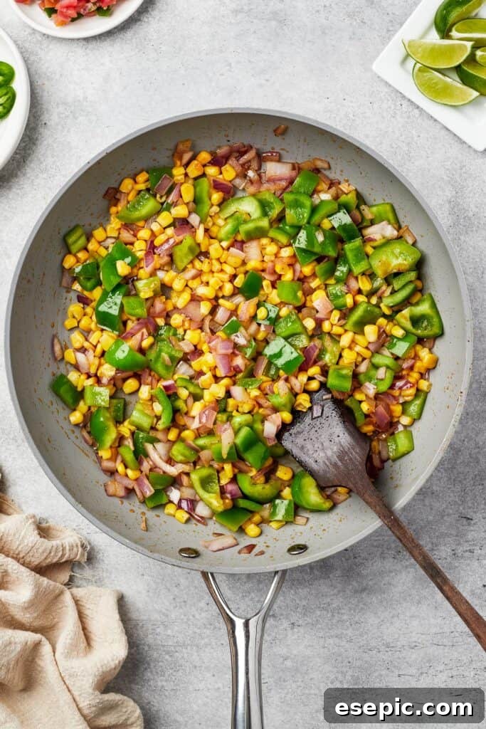 Chopped corn, vibrant bell pepper, and sliced onion cooking together in a skillet, softening and blending flavors.
