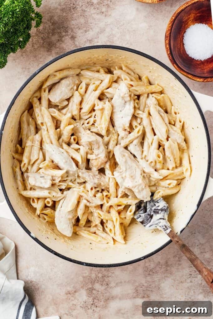Cooked chicken, pasta, and creamy Alfredo sauce combined in a large pot, ready for transfer to a baking dish.