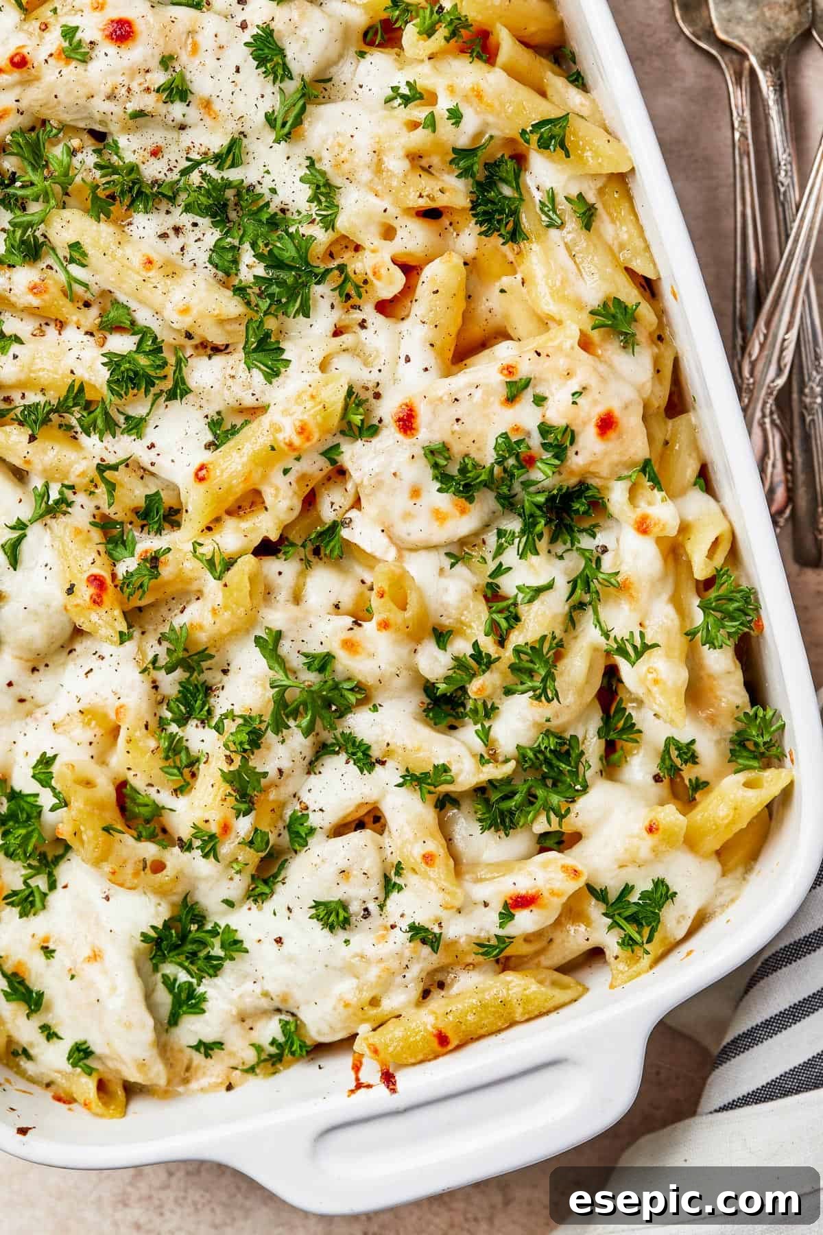 A baked chicken and pasta casserole, generously garnished with fresh chopped parsley, served directly from the baking dish.