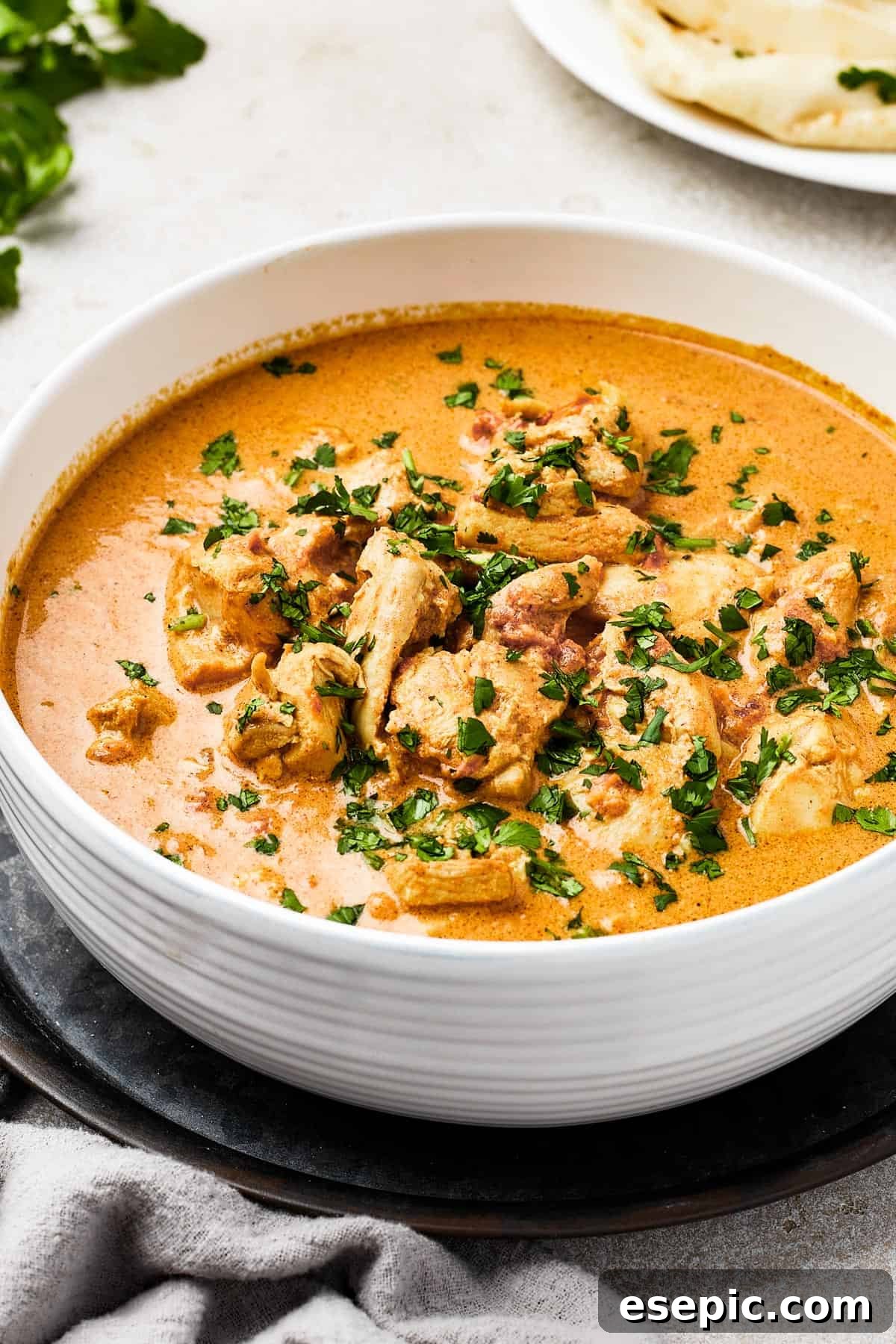 Classic Indian Butter Chicken, a creamy chicken curry in a white enamel bowl, garnished with fresh cilantro.