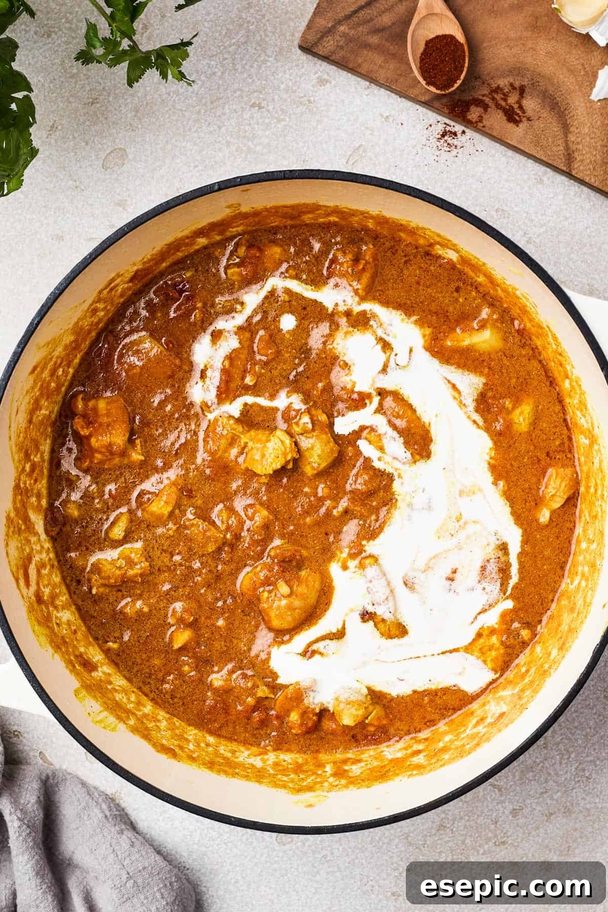 A heavy pot showcases chicken simmering in a vibrant tomato sauce, with heavy cream being delicately poured over it, adding to its richness.