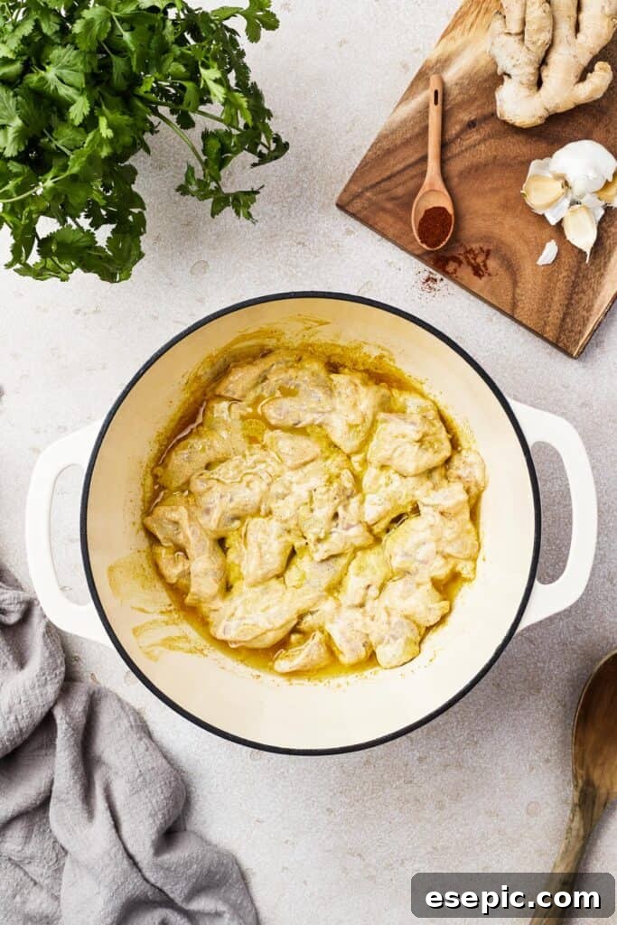 Chicken cooking in a rich, yellow-orange creamy sauce, absorbing all the aromatic flavors.