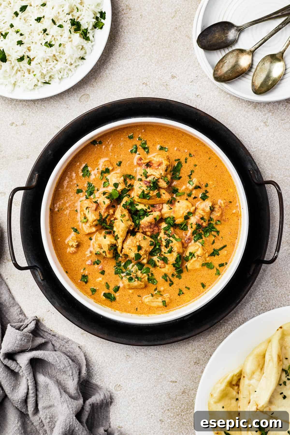 Overhead view of a white enamel dish filled with creamy Indian Butter Chicken, elegantly resting on a cast-iron holder and garnished with fresh cilantro.