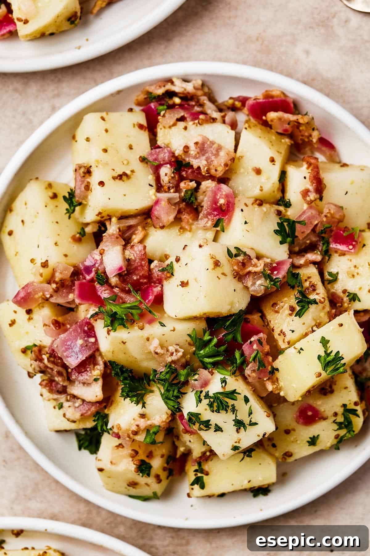 Warm German Potato Salad with Bacon 3 Overhead shot of several small plates, each with a serving of warm German potato salad, garnished with fresh herbs, showcasing its appetizing presentation.