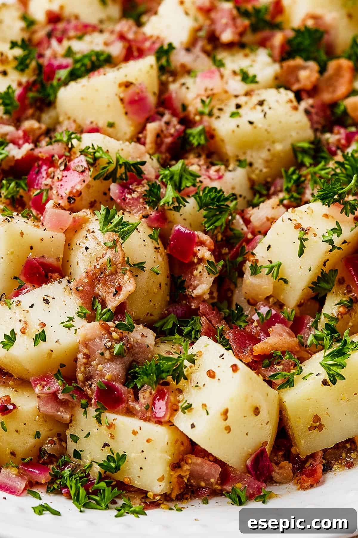 Warm German Potato Salad with Bacon 10 Close-up shot of a generous portion of German potato salad on a white serving dish, garnished with fresh herbs and a hint of bacon.
