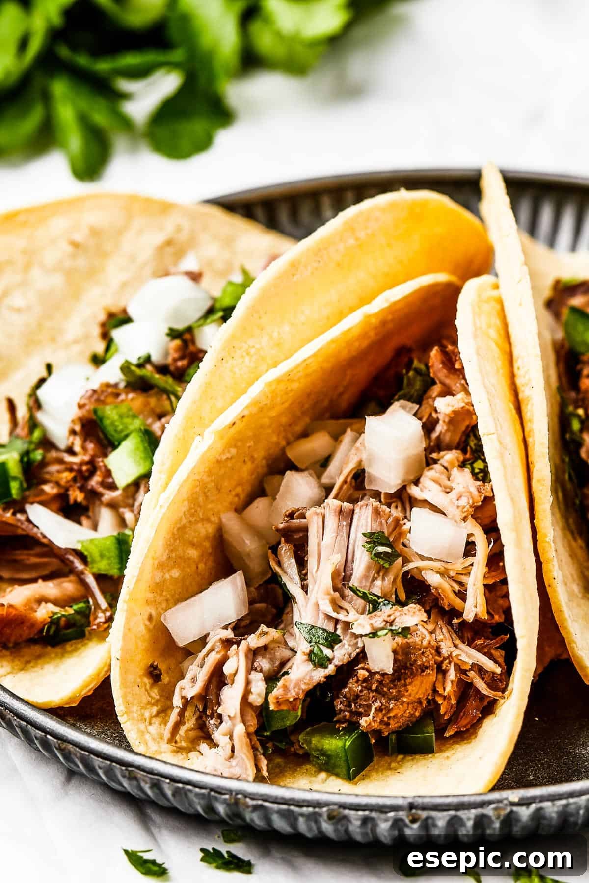 Close-up shot of three pork tacos with onion and herbs, showcasing crispy carnitas.