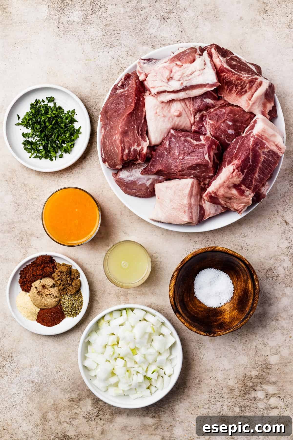A flat lay of ingredients for slow cooker pork carnitas including chopped cilantro, pork butt, orange juice, lime juice, various seasonings, salt, and white onion.