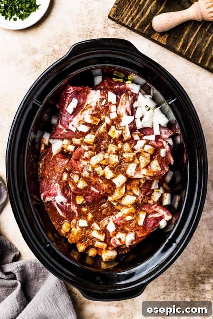 Chunks of pork and diced onion nestled in a slow cooker, generously topped with a spiced liquid blend.