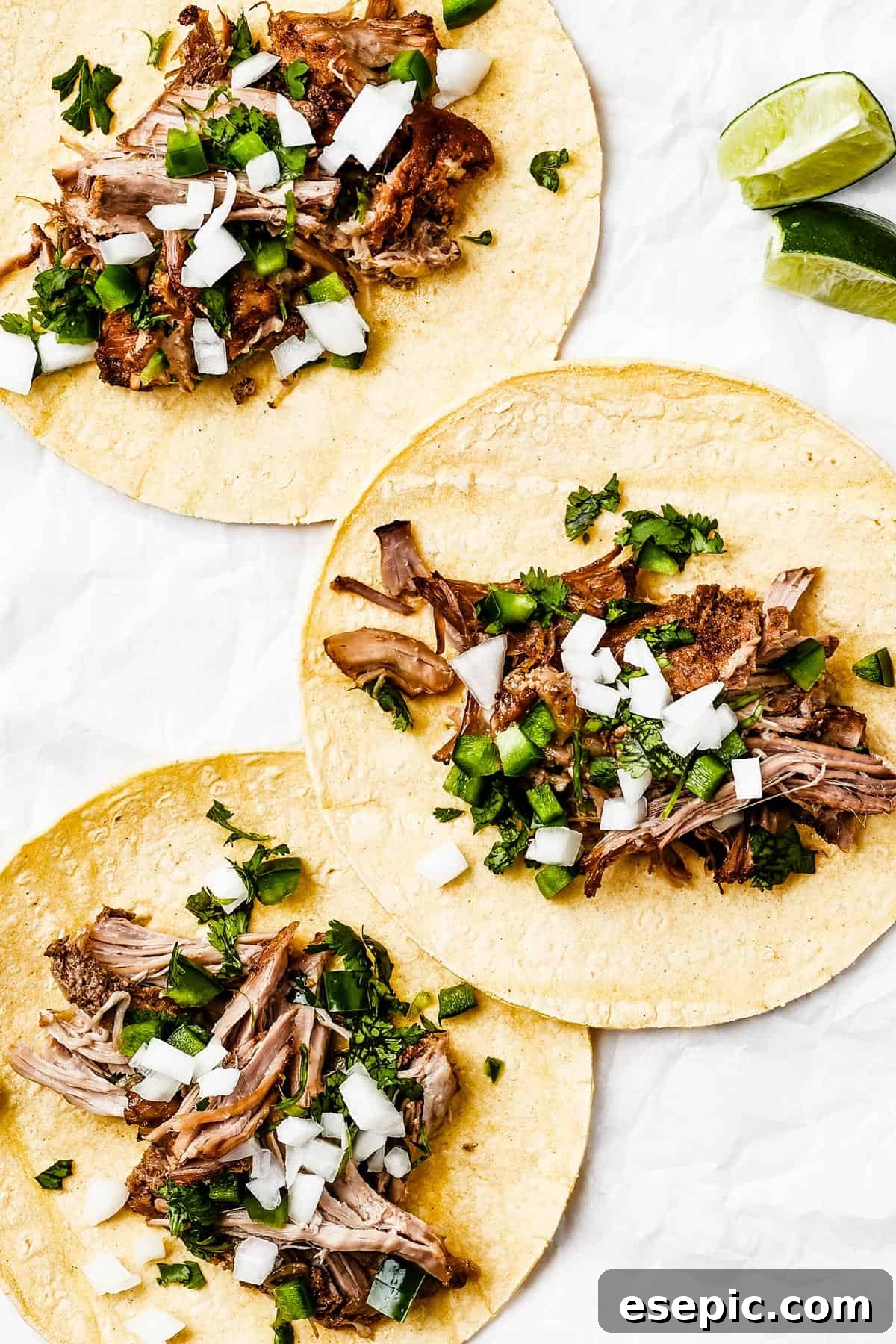Three perfectly prepared tortillas, each filled with shredded pork and an array of fresh toppings in the center.